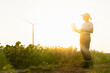 © scharfsinn86 - Woman farmer wearing white cap and t-shirt with laptop. Wind turbines in the background