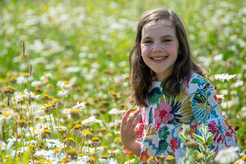 Happy little blonde girl sniffs a bunch of daisies in summer at sunset. High quality photo