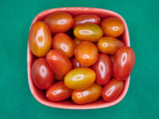 Wall Mural - Red and yellow cherry tomatoes in a glass bowl on a green background