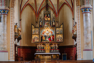 An ornate church altar with religious artwork, statues, candles, and detailed architecture, featuring a colorful depiction of a biblical scene..