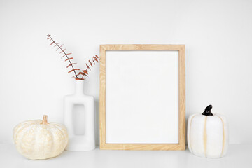 Poster - Mock up portrait wooden frame with fall branches and pumpkin decor on a white shelf against a white wall. Autumn concept. Copy space.