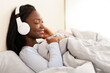 © Prostock-studio - Relaxed Afro Girl In Wireless Headphones Listening To Music Lying In Bed At Home. Panorama, Empty Space, Selective Focus