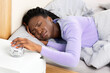 © Prostock-studio - Afro Lady Turning Off The Alarm-Clock Having A Hard Time Waking Up In The Morning Lying In Bed At Home