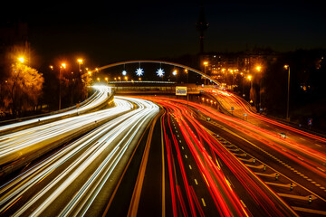 Traces of car lights at dusk driving along the Madrid ring road with the Piruli in the background