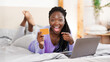 © Prostock-studio - Excited Black Girl Shopping Online With Laptop Pointing Finger At Credit Card Lying In Bed At Home. Selective Focus