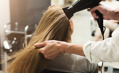 stylist making hairstyle using hair dryer, blowing on wet customer hair at beauty salon, copy space