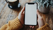 © Elnare - Close up of woman's hands holding a smartphone with a blank screen in a cafe setting.