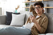 © Prostock-studio - Enjoying Weekend. Handsome Asian Man In Glasses Using Smartphone While Sitting Leaning On Couch At Home, Happy Guy Relaxing In Living Room, Browsing Internet Or Messaging With Friends, Selective Focus