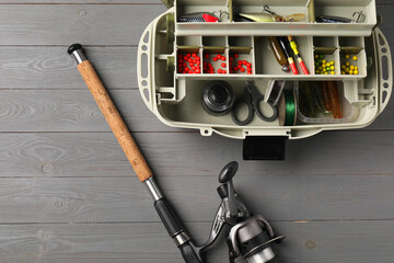 Sticker - Different fishing tackles in box and rod with spinning reel on grey wooden table, top view. Space for text