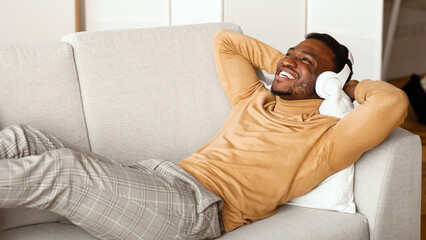 Poster - Relax. Happy Afro Man In Wireless Headphones Listening To Music Lying On Sofa At Home