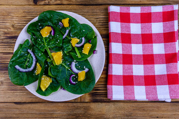 Wall Mural - Salad with spinach leaves, pieces of orange, sesame seeds and onion in a ceramic plate. Top view