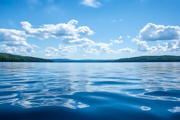 Wall Mural - Calm blue lake water surface with hills in the background and a blue sky with clouds