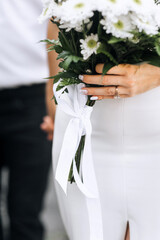 Wall Mural - Close-up wedding photo of a bouquet of chrysanthemum flowers with a white ribbon in the hands of a bride with a gold ring on her finger.