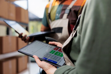 Stockroom colleagues analyzing inventory report on tablet computer, working at clients orders before shipping packages in warehouse. Diverse supervisors looking at merchandise checklist. Close up