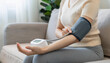 © anandart - Hypotension problem, close up hand young woman sitting on couch high check blood pressure heart rate with digital pressure monitor, making self check up pulse on arm, cuff at home. Healthcare medical