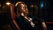 © Iona - A young woman in an elegant suit rests on an armchair in a dimly lit room, exuding sophistication and tranquility.