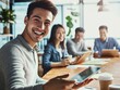 © 为轩 张 - Smiling young man with an iPad at a conference table, surrounded by casually dressed colleagues in a bright, modern office space with documents and coffee cups.