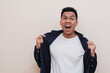 © Nurma - A happy Southeast Asian man wearing shouts while holding his shirt, Yes, I did it! Success concept