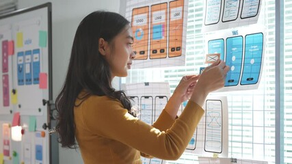 Wall Mural - young asian woman working as ux or ui designer is arranging pieces of paper representing wireframe p
