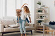 © SHOTPRIME STUDIO - Joyful mother and daughter dancing together in a cozy living room with a comfortable couch in the background