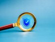 © tete_escape - Cybersecurity, digital data and information online protection technology concept. Shield padlock icon in golden magnifying glass lens, isolated on net grid and blue background, minimal style.