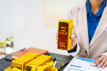 An Asian businesswoman is sitting at her desk, discussing gold bars, deposits,and the gold market with investors.She analyzes gold price trends highlights the long-term benefits of investing in gold