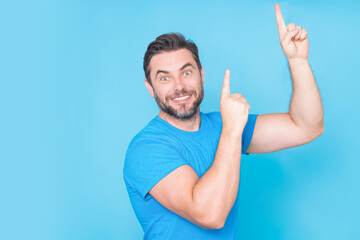 The point up. Look up. Happy handsome man pointing up away, isolated blue background. Excited man pointing a great idea. Guy in blue t-shirt pointing up with his finger.