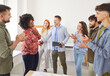 © Studio Romantic - Young woman shaking hands with man celebrating success, making deal, business achievement or signing contract with group of young people standing in a circle in office on meeting and applauding.