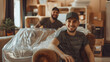 © SS Digital - Portrait of a two young smiling male movers packing furniture in the living room. Moving service men workers wrapping chair with plastic wrap. Move, moving day and relocation concep