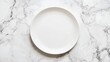 © CreativeBro - Empty white round plate displayed on a marble surface from a top view