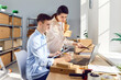 © Studio Romantic - Young colleagues working at workplace in storeroom checking stock and inventory on a laptop. Company employees preparing order in storeroom in retail warehouse full of cardboard boxes.