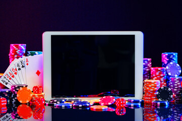 A gaming tablet surrounded by colorful poker chips at a casino table during a night gambling session