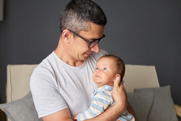 Handsome Caucasian dad holding newborn daughter smiling and caring for baby enjoying precious childhood moments while caring for newborn son sitting on couch