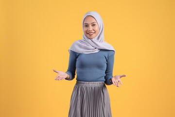 Wall Mural - asian indonesian muslim woman with presenting hand gesture on isolated yellow background