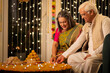 © G-images - Happy Senior couple decorating with Diya on the occasion of Diwali festival celebration.