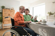 © Westend61 - Senior man on wheelchair sitting with wife using digital PC at home