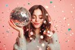 © gankevstock - Happy woman holding a disco ball with confetti falling around on a vibrant pink background