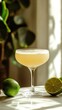 © isti - A refreshing yellow cocktail in a coupe glass with lime wedges and a green plant in the background.