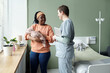 © pressmaster - Smiling mother holding newborn baby while having conversation with a healthcare professional in a hospital room. Scene includes potted plants and a hospital bed
