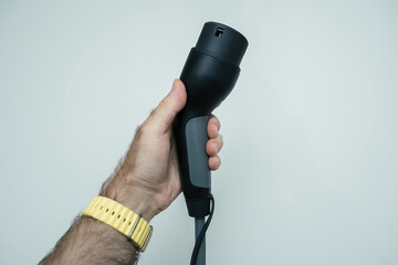 A male hand holds an EV charging cable with a close-up view of marram grass in the sand dunes of the Netherlands