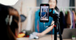 © Johnstocker - Selective focus on mobile phone of Cheerful woman influencer is live streaming sell clothes on social media or blogging in home studio. Remote buying, Online shopping, Sell ​​products online