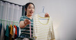 © Johnstocker - Portrait of Cheerful woman influencer is live streaming to sell clothes and measuring the sizes of clothes for customers who inquired on social media in home studio. Remote buying.