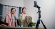 © Johnstocker - Low angle view, Two cheerful woman influencers are live streaming sell clothes on social media or blogging in home studio. Remote buying, Online shopping, Sell ​​products online