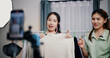 © Johnstocker - Portrait of Two cheerful woman influencers are live streaming sell clothes on social media or blogging in home studio. Remote buying, Online shopping, Sell ​​products online