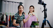 © Johnstocker - Selective focus, Two cheerful woman influencers are live streaming selling clothes and pressed a bell to attract customers' attention in home studio. Remote buying, Online shopping.