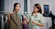 © Johnstocker - Portrait of Two cheerful woman influencers are live streaming to sell clothes and measuring the sizes of clothes for customers who inquired on social media in home studio. Remote buying.