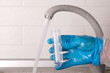 © Alsu - Analysis of tap water in the house, hand in blue glove draws water into a test tube from the tap for laboratory test, close-up