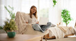 © My Ocean studio - Beautiful young woman sits comfortably in a bright, modern room, working on a laptop. She is seated in a cozy chair with a blanket, surrounded by greenery, natural light, and a relaxed atmosphere.