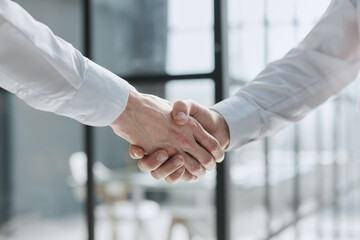 Two businessmen shake hands on the background of empty modern office, signing of a contract concept, close up