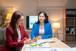 © Wasana - Two women in suits are sitting at a table with papers and a projector